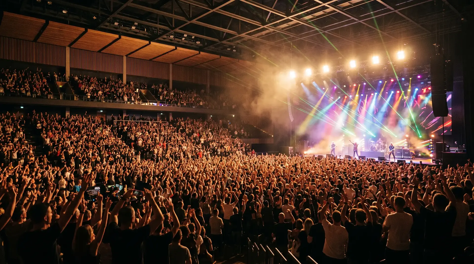 Packed indoor arena during a live show, with colorful stage lights and the crowd seen from behind facing the stage